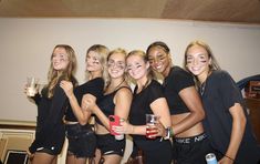 a group of young women standing next to each other holding drinks and posing for the camera