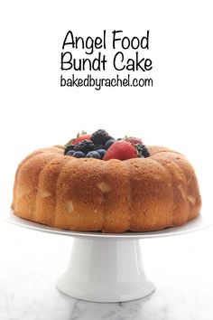 an angel food bundt cake topped with berries and blueberries on a white pedestal