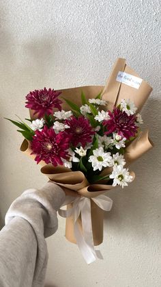 a person holding a bouquet of flowers in front of a white wall with a brown ribbon