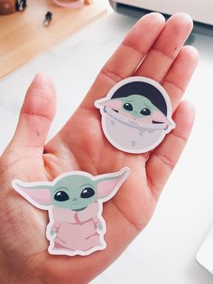 two stickers in the palm of someone's hand, one with a baby yoda on it