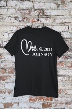 "Custom Designed \"Mr. and Mrs.\" T-Shirts Personalized for you with last name (ALL CAPS) and year established. White T-Shirts imprinted in Black. Black T-Shirts imprinted in White. T-Shirts are Gildan 100% Soft Cotton, the industry's favorite for imprinting. Select color and size for each - SOLD IN PAIRS ONLY. Provide us with LAST NAME and YEAR in Personalization Section." Anniversary Graphic Tee With Letter Print, Black Letter Print T-shirt For Anniversary, Short Sleeve Tops With Name Print For Anniversary, Black Graphic Tee For Anniversary, Black Graphic Print T-shirt For Anniversary, Black Cotton T-shirt For Anniversary, Pre-shrunk Cotton T-shirt For Anniversary, Cotton Anniversary T-shirt With Text Print, Cotton T-shirt With Text Print For Anniversary