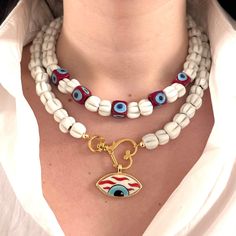 This exquisite double layer necklace features a beautiful combination of artisan-made glass beads and handcrafted ceramic evil eye pendants, creating a unique and eye-catching design. One layer includes elegant glass cube evil eye beads, while the other showcases a stunning ceramic evil eye pendant set in a 24kt gold plated bezel. Both layers are adjustable with two-inch extender chains, making it easy to find the perfect length for your style. Wear them together for a layered look or separately to mix and match with other jewelry pieces. At a base length of 14 inches, this necklace is versatile and can be worn with a variety of necklines, making it a perfect addition to any jewelry collection. Handmade with care and attention to detail, this necklace is truly one of a kind and a beautiful Handmade White Double Strand Jewelry, Double Strand Glass Necklaces As Gift, Double Strand Glass Necklaces For Gift, Double Strand Glass Necklace As Gift, Spiritual White Jewelry With Evil Eye, Handmade Double Strand Beads For Gifts, Handmade Double Strand Beads As Gift, Handmade Double Strand Beads For Gift, Adjustable White Beaded Necklace With Evil Eye