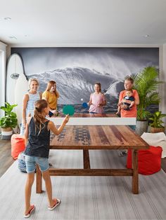 children playing ping pong on a wooden table in front of a large wall mural