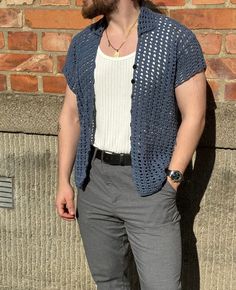 a man standing in front of a brick wall wearing a blue crochet cardigan