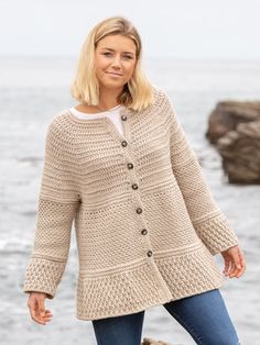 a woman standing on the beach wearing a cardigan sweater and jeans with her hands in her pockets