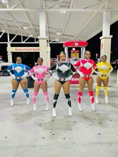 four women dressed in costume standing next to each other at a gas station, posing for the camera