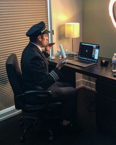 a man sitting at a desk in front of a laptop computer wearing a pilot's hat