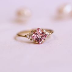 a pink diamond ring sitting on top of a white table next to pearl beads and pearls