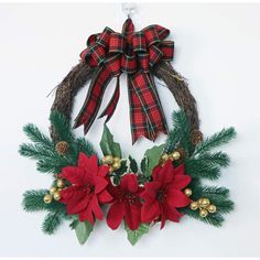 a christmas wreath with poinsettis and pine cones hanging on a white wall