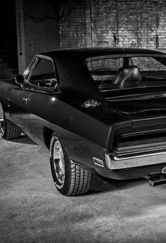 a black and white photo of a muscle car parked in a garage next to a brick wall