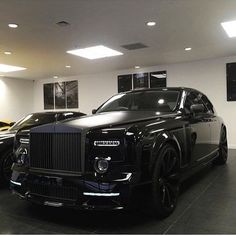 two black rolls royces are parked in a showroom with white walls and ceiling lights