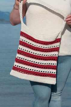 a woman carrying a crocheted red white and blue bag on her back with the ocean in the background