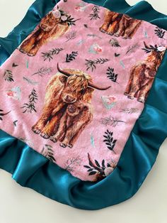 a blanket with highland cattle on it is laying on a blue satin pillow and cover