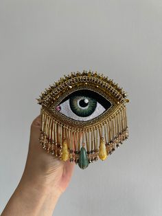 a hand holding an eye shaped brooch with beads and chains around it's eyes