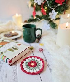 a crocheted christmas ornament sits next to a book and candle on a white table