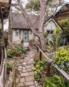 a stone path leads to a small cottage with flowers in the foreground and potted plants on either side