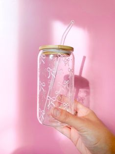 a hand holding a mason jar with a straw in it on a pink wall background