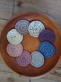 a wooden bowl filled with crochet coasters on top of a wooden table