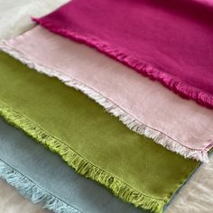 four different colored scarves on top of each other with fringes around the edges