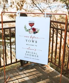 a sign that is hanging on a fence with flowers and wine glasses in the background