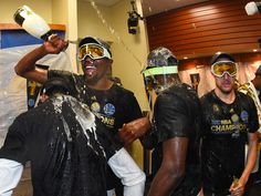 three men in black shirts and goggles are spraying water on each other while one man is holding a bottle