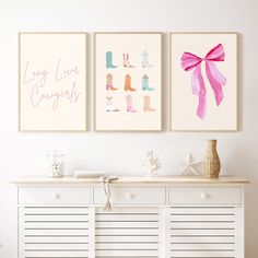 two pink and white prints on the wall above a dresser with drawers, vases and other items