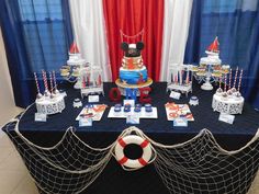 a table topped with lots of cakes and desserts next to a red white and blue curtain