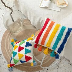 two colorful pillows sitting on top of a table next to a glass vase and plate