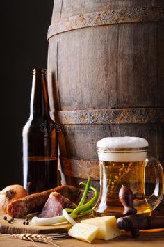 beer, cheese and meat are sitting on a table next to a barrel with two bottles