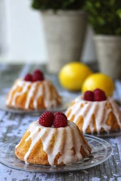 two small cakes with raspberries and icing sitting on a table next to lemons