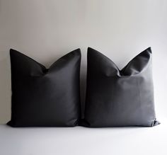 two black pillows sitting next to each other on top of a white surface with no one in it