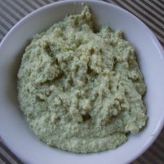 a white bowl filled with green food on top of a striped tablecloth covered table