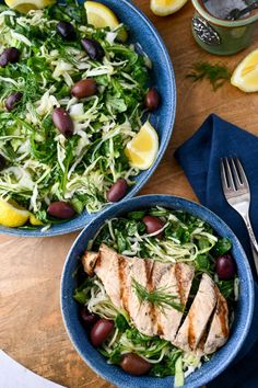 two blue bowls filled with salad on top of a wooden table next to silverware