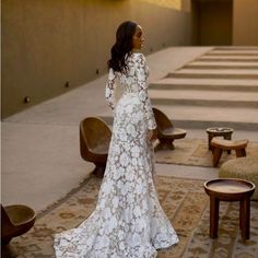 a woman in a white wedding dress standing on a rug with chairs and tables behind her