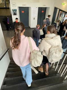 two girls are walking down the stairs with their bags on their back and one girl is carrying another bag