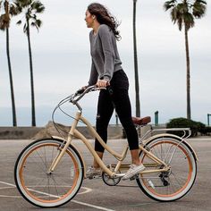 a woman riding a bike in a parking lot with palm trees and sky behind her