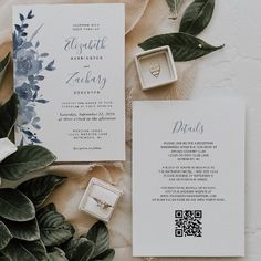 the wedding stationery is laid out next to some greenery and rings on display