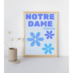 there is a vase with flowers in it next to a framed poster that says, notre dame indiana