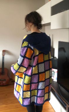 a woman standing in front of a tv wearing a colorful crocheted sweater