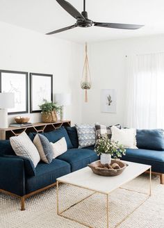 a living room with blue couches and pillows on the floor, white walls and ceiling fan