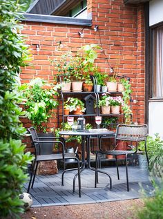 an outdoor table and chairs with potted plants on the wall in front of it