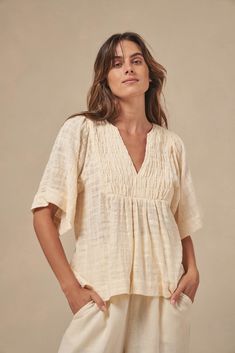 The Tulum top from Australian brand Little Lies is a perfect staple for spring/summer. Features pleated detail on the front, a flattering square sleeve and a v-neckline. This gorgeous top is an oversized fit that can be paired with your favorite pants or shorts. Semi-sheer. Materials: 100% Cotton Care: Wash with like colors; cold gentle machine wash; do not bleach; lay flat to dry; warm iron; do not tumble dry. Size Info: Model is 5'8" and is wearing a size S; relaxed fit Size Guide | Shipping Policy Beige V-neck Top For Summer, Versatile Beige V-neck Blouse, Effortless V-neck Blouse For Day Out, Versatile V-neck Blouse For Beach, Versatile Beige V-neck Top, Relaxed V-neck Blouse For Day Out, Chic Spring Top With Notched Neckline, Chic Tops With Notched Neckline For Spring, Spring Top With Notched Neckline For Day Out