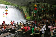 many people are sitting at picnic tables in front of a waterfall with stars hanging from the ceiling