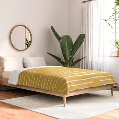 a bed sitting in a bedroom next to a mirror and potted plant on top of a wooden floor