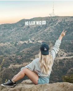 a woman sitting on top of a rock with her arms in the air and hollywood sign behind her