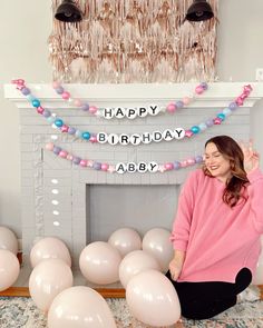 a woman sitting on the floor in front of balloons and a birthday cake with candles