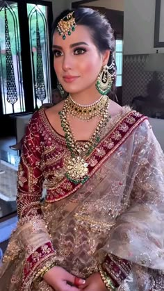 a woman in a red and gold bridal outfit with jewelry on her head, posing for the camera