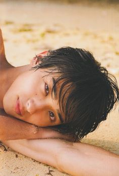 a woman laying on top of a sandy beach next to the ocean with her hair blowing in the wind