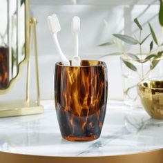 two toothbrushes sitting in a cup on a marble table next to a mirror