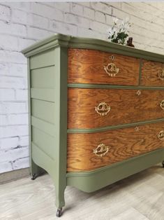 a green dresser with gold handles and knobs on the bottom drawer, in front of a white brick wall